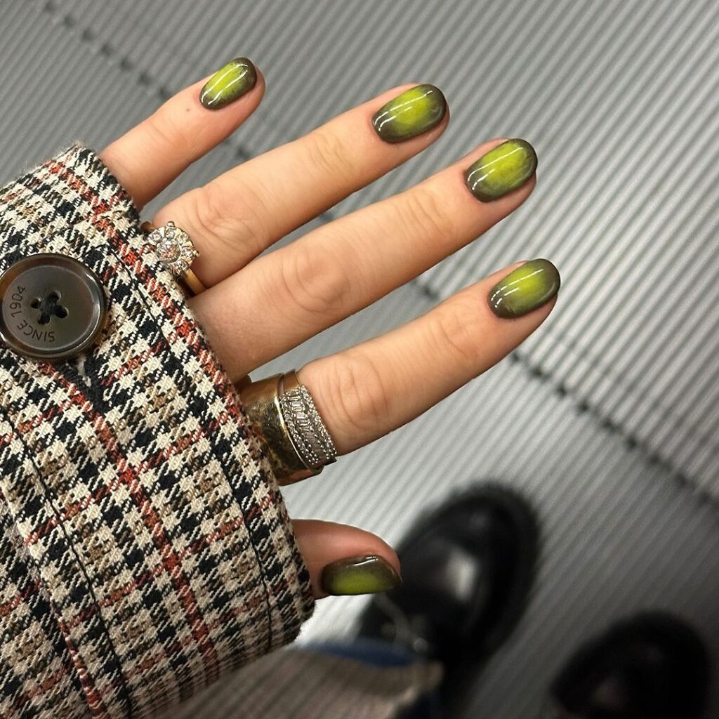 Mão de pele branca, com anéis em dourado e unha curta redonda com design aura 
