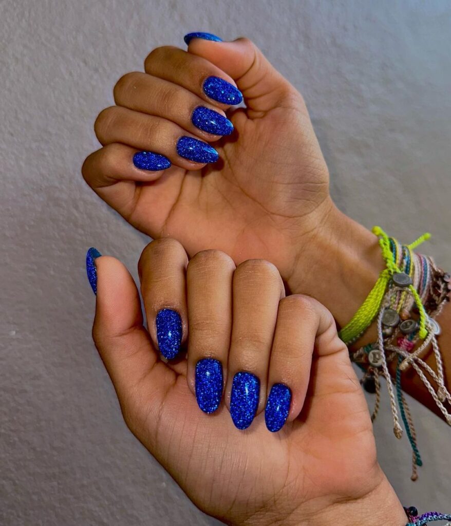 Mãos de pele preta com unha amendoada azul com glitter