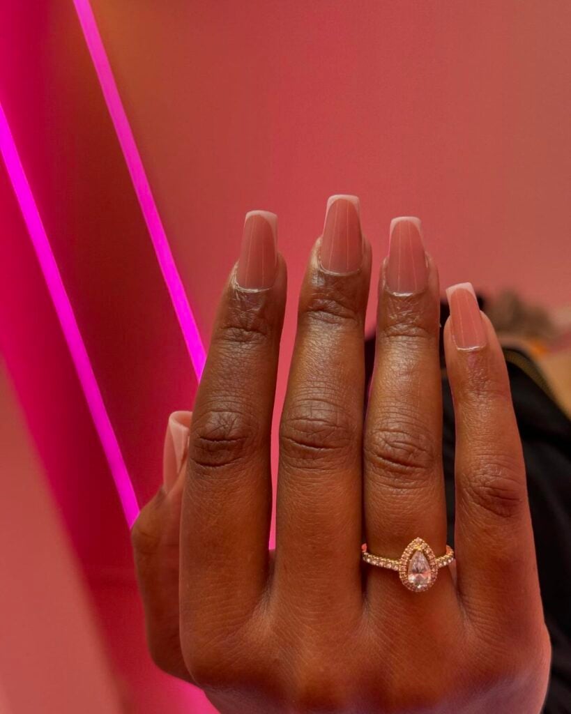 Mão de pele preta, com anel prata e unha bailarina rosa-claro com francesinha rosa