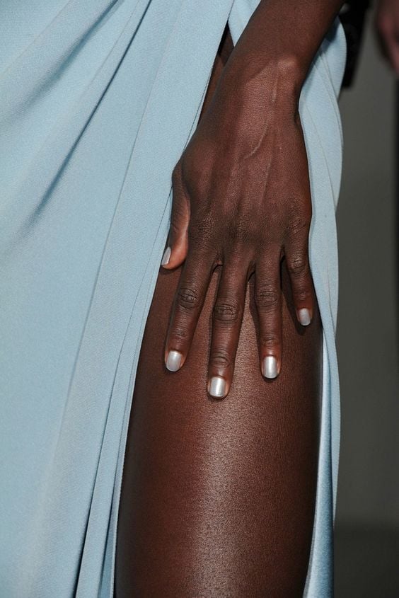 Mão de pele preta, apoiada na perna com unha arredondada branca perolada Like Magazine
