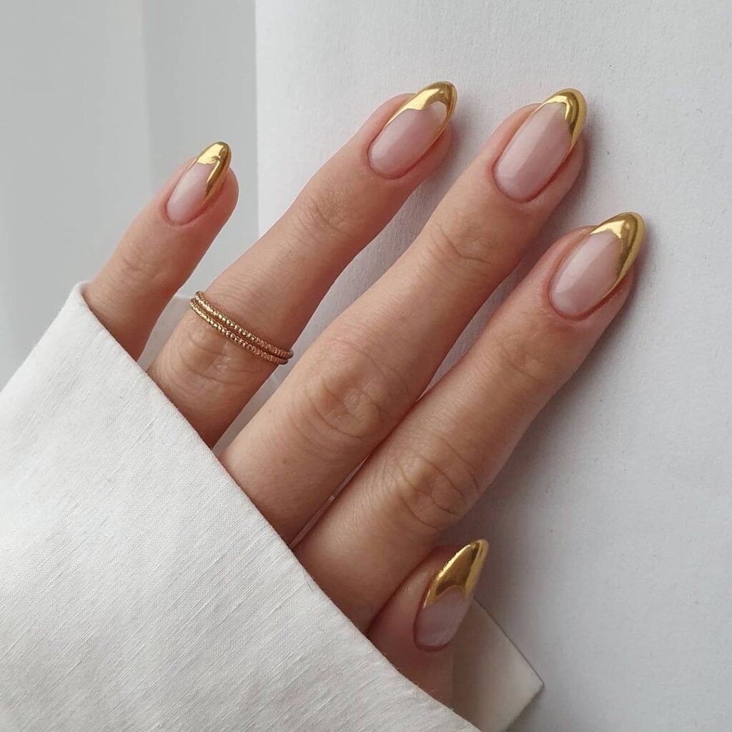 Mão de pele branca, com anel dourado e unha amendoada com francesinha dourada orgânica