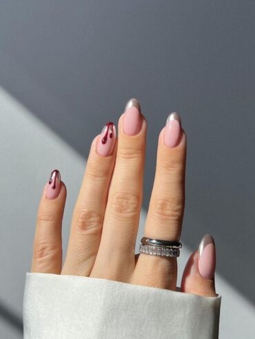 Mão de pele branca, com anéis e unha amendoada com francesinha metalizada e gotas de sangue