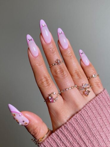 Mão de pele branca, com anéis de brilhante e unha amendoada com francesinha rosada com strass de borboleta