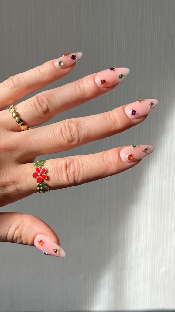 Mão de pele branca, com anéis e unha stiletto com strass coloridos