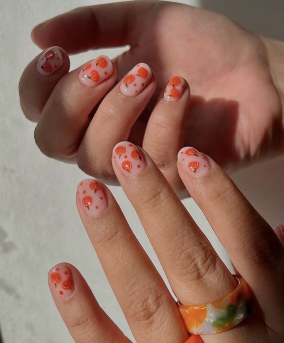 Mãos branca com anel colorido e unha curtinha com estampa de abóbora 