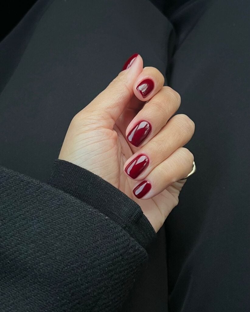 Mão de pele branca com unha curta e quadrada vermelho-escuro