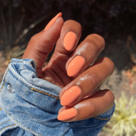 Mão de pele preta curvada com unha curta stiletto pêssego