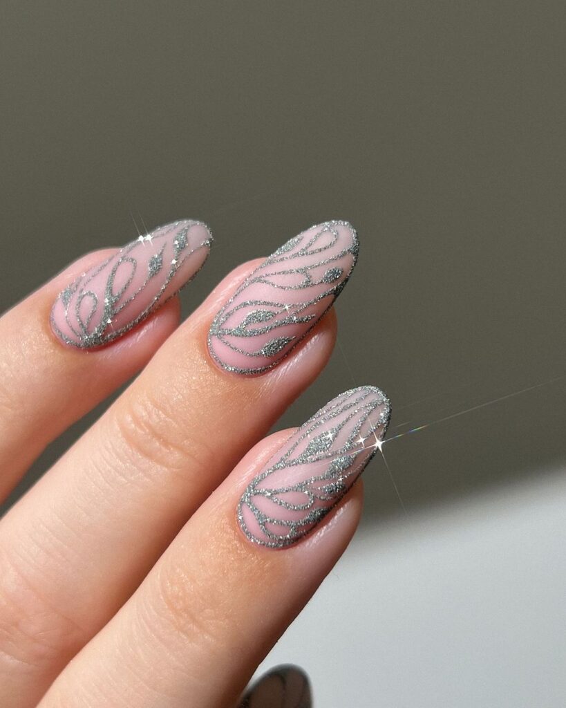 Mão de pele branca, com unha amendoada nude decorada com glitter prata