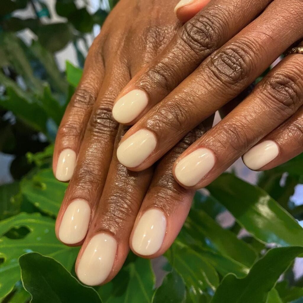 Mão de pele negra, com unha curta e redonda, com esmalte amarelo-manteiga em tom pastel