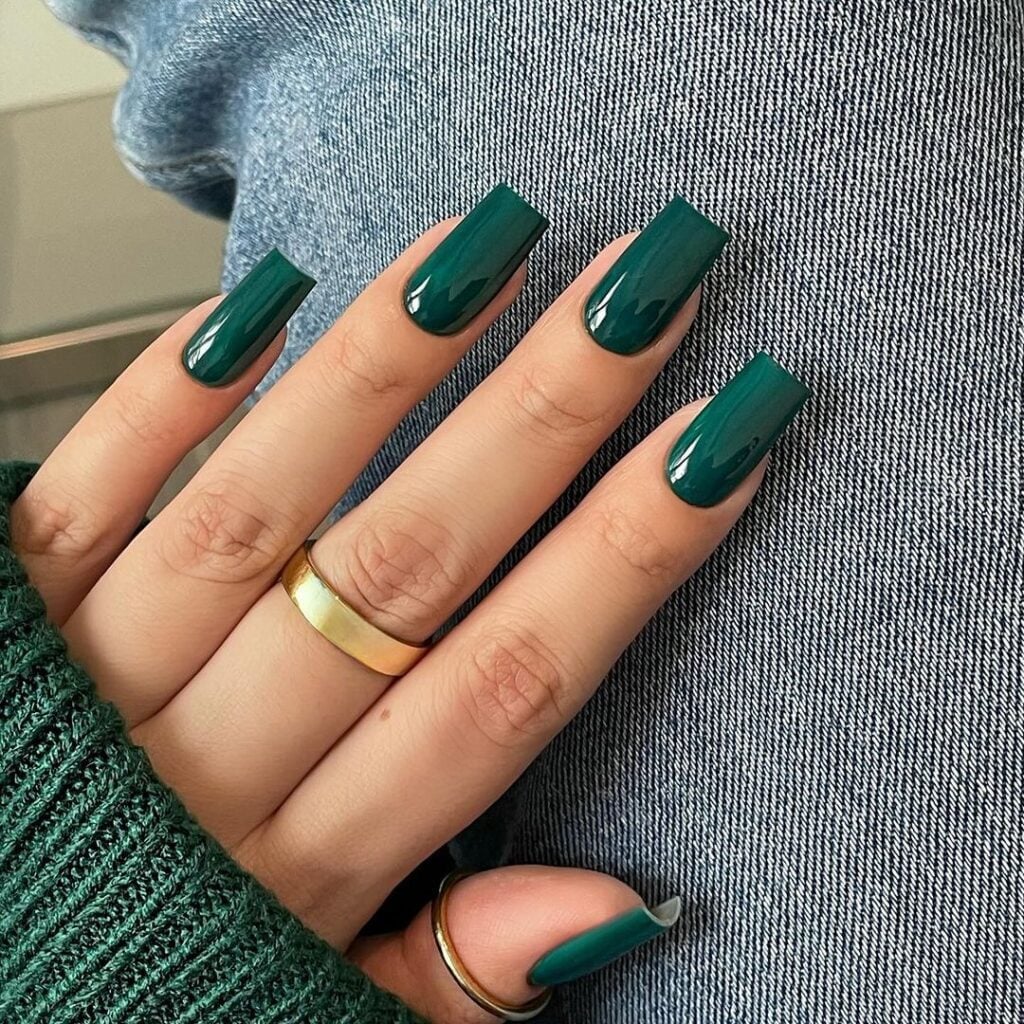 Mão de pele branca, com anel dourado e unha quadrada verde-esmeralda 