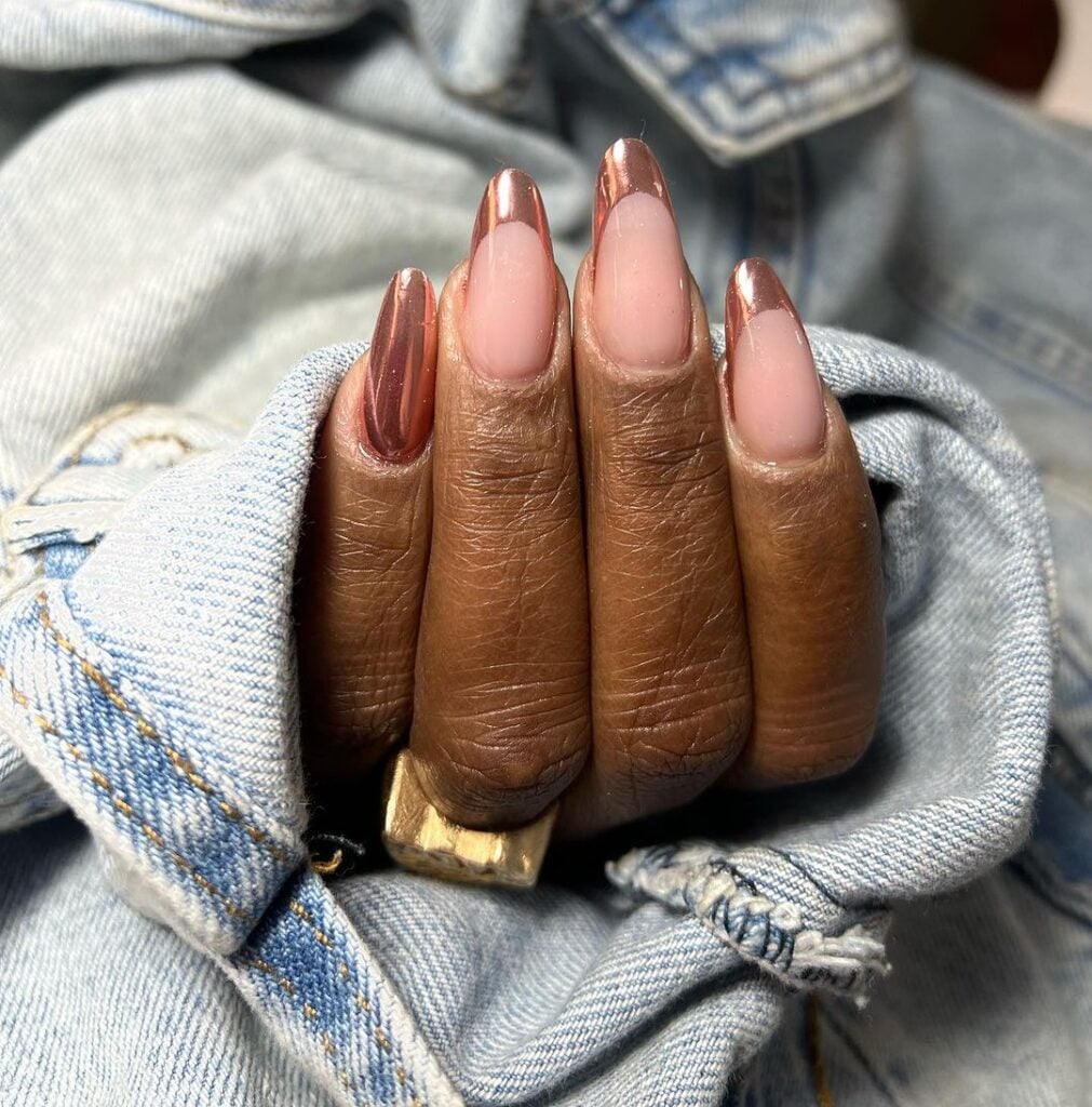 Mão de pele preta, com anel dourado e unha amendoada com francesinha rosé metalizada