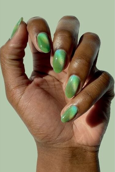 Mão de pele preta meio fechada com unha stiletto verde magnético
