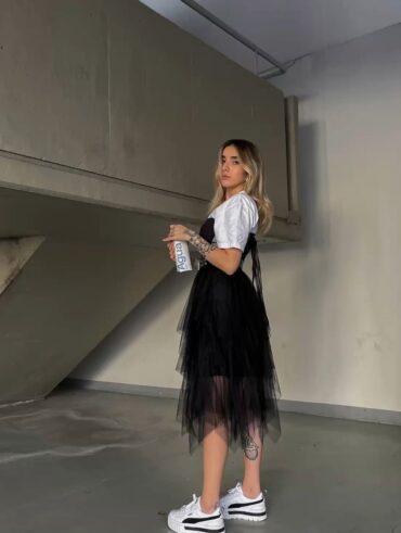 Mulher jovem, magra e loira, usando camiseta branca e uma saia preta de tule com tênis
