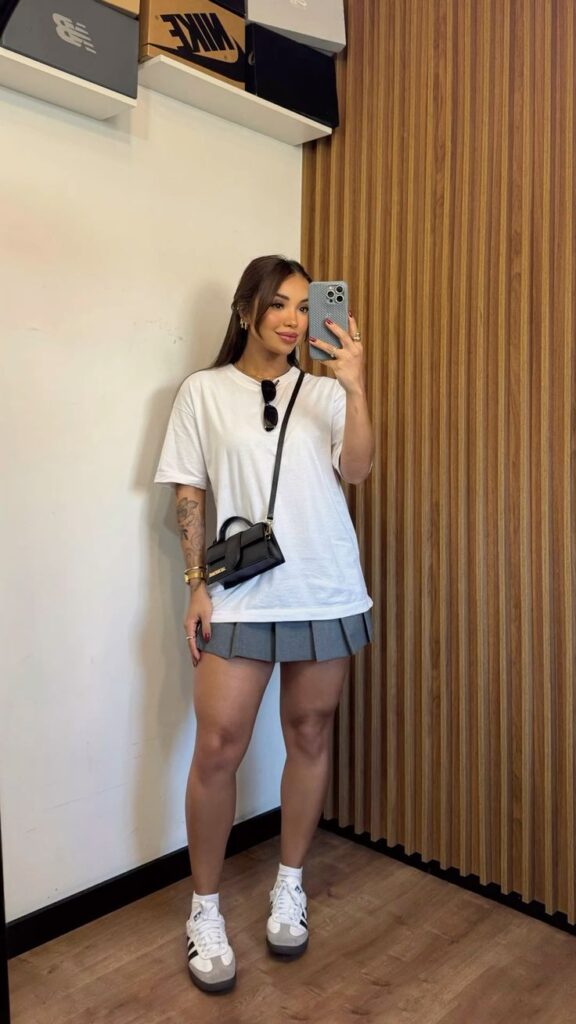 Look com camiseta branca, saia plissada em cor cinza e Adidas Samba