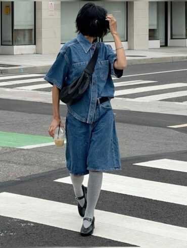 Mulher jovem, magra e de pele clara. Ela usa conjunto jeans, meia cinza e sapato preto.