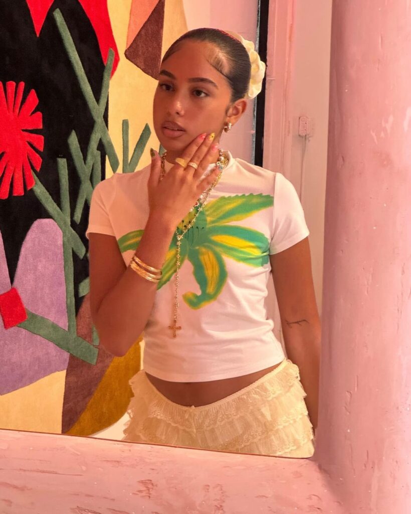 Mulher jovem, magra e de pele escura. Ela usa camiseta com estampa de flor.