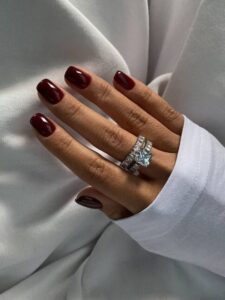 Mão de pele branca, com anéis em prata e unha curta e quadrada vinho