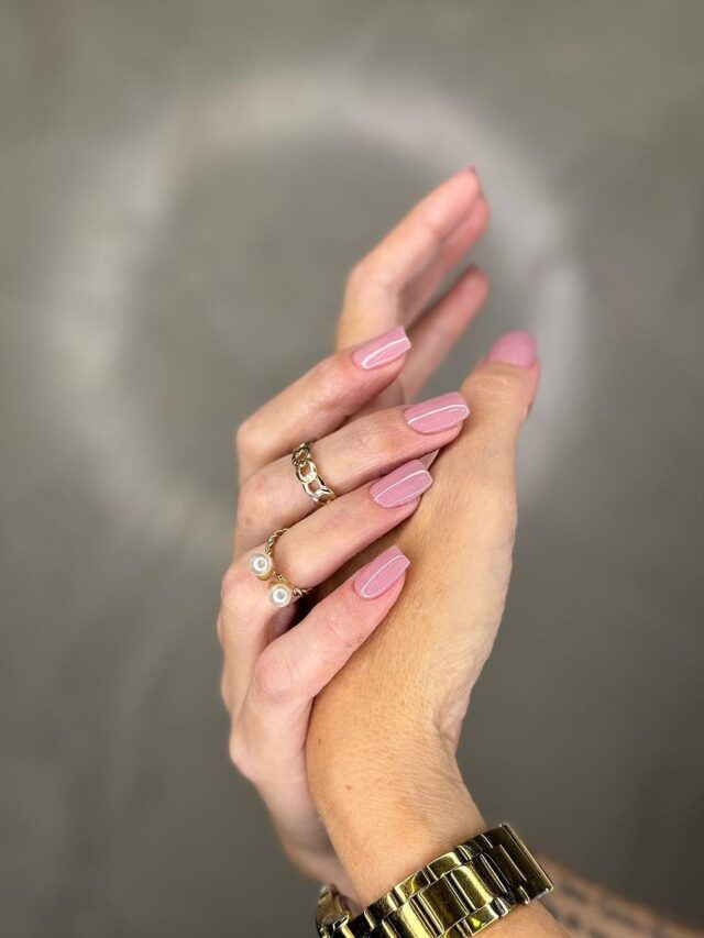 Mãos de pele branca, entrelaçadas, com anéis e unha quadrada rosa-claro