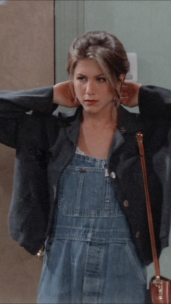 Rachel Green do seriado Friends usando look com jardineira jeans e casaco.