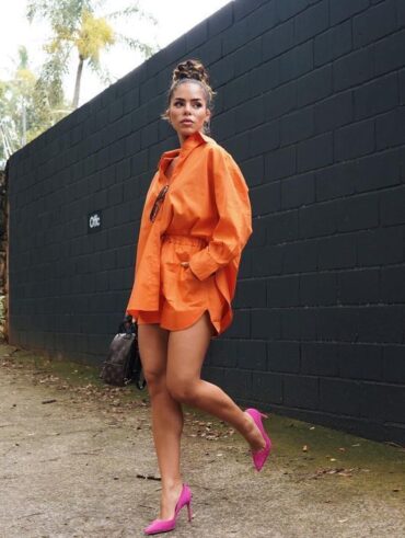 Mulher jovem, usando coque no cabelo, conjunto de camisa e short laranja com sapato de salto em cor rosa