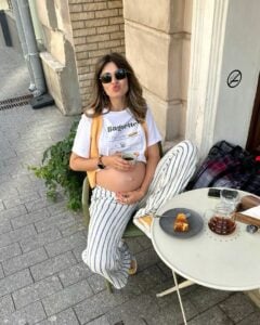 Mulher jovem e magra com pele clara. Ela usa camiseta e calça listrada.
