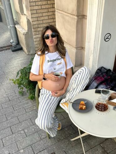 Mulher jovem e magra com pele clara. Ela usa camiseta e calça listrada.