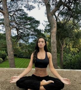 Mulher jovem e magra sentada com perna cruzada e praticando meditação.