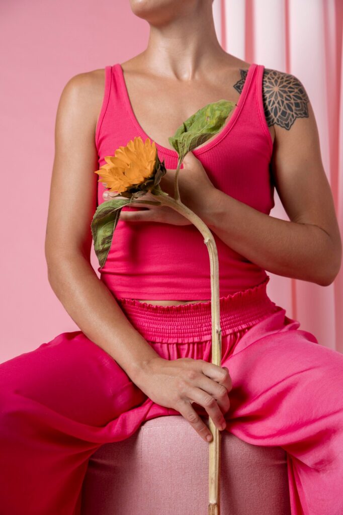 Tronco de uma mulher em campanha contra o câncer de mama; ela usa regata e calça rosa e está segurando uma flor.