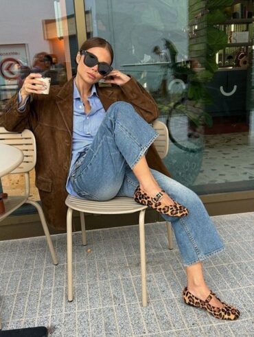 Mulher jovem magra e de pele clara. Ela usa look com camisa azul e sapatilha de oncinha.