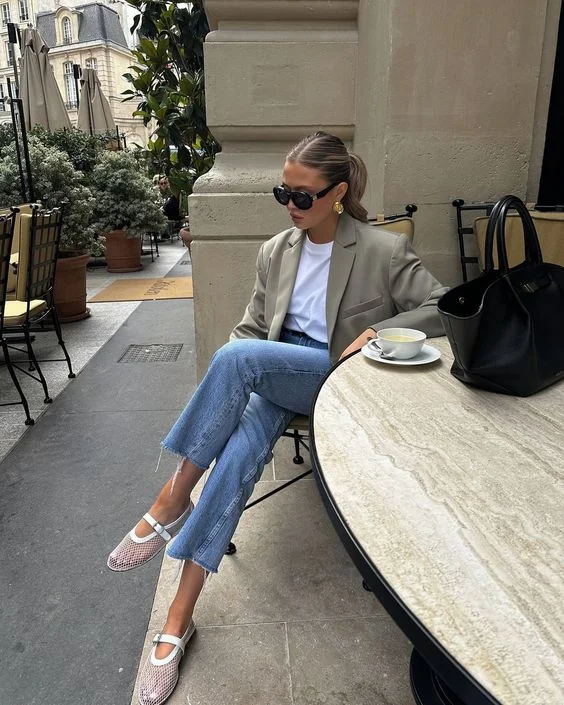 Mulher jovem, magra e de pele clara. Ela está com blazer, blusa, calça jeans e sapatilha em tela.