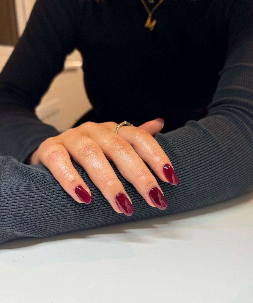 Mão de pele branca, com unha média e amendoada, com esmalte vermelho escuro