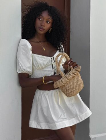 Mulher jovem e magra de pele escura. Ela está usando um vestido branco curto.