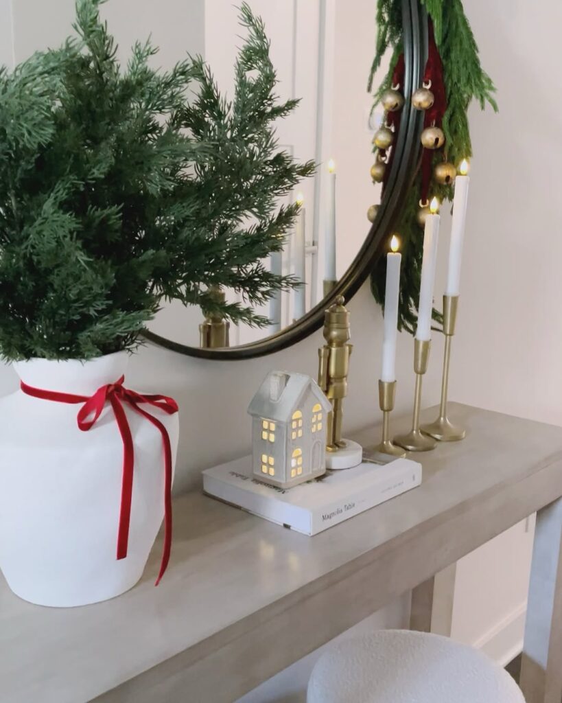 Aparador com decoração natalina, com casa enfeitada, vaso de plantas com laço, livro e velas