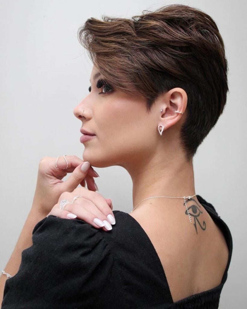 Mulher branca com cabelo bixie, liso e castanho, usando acessórios em prata