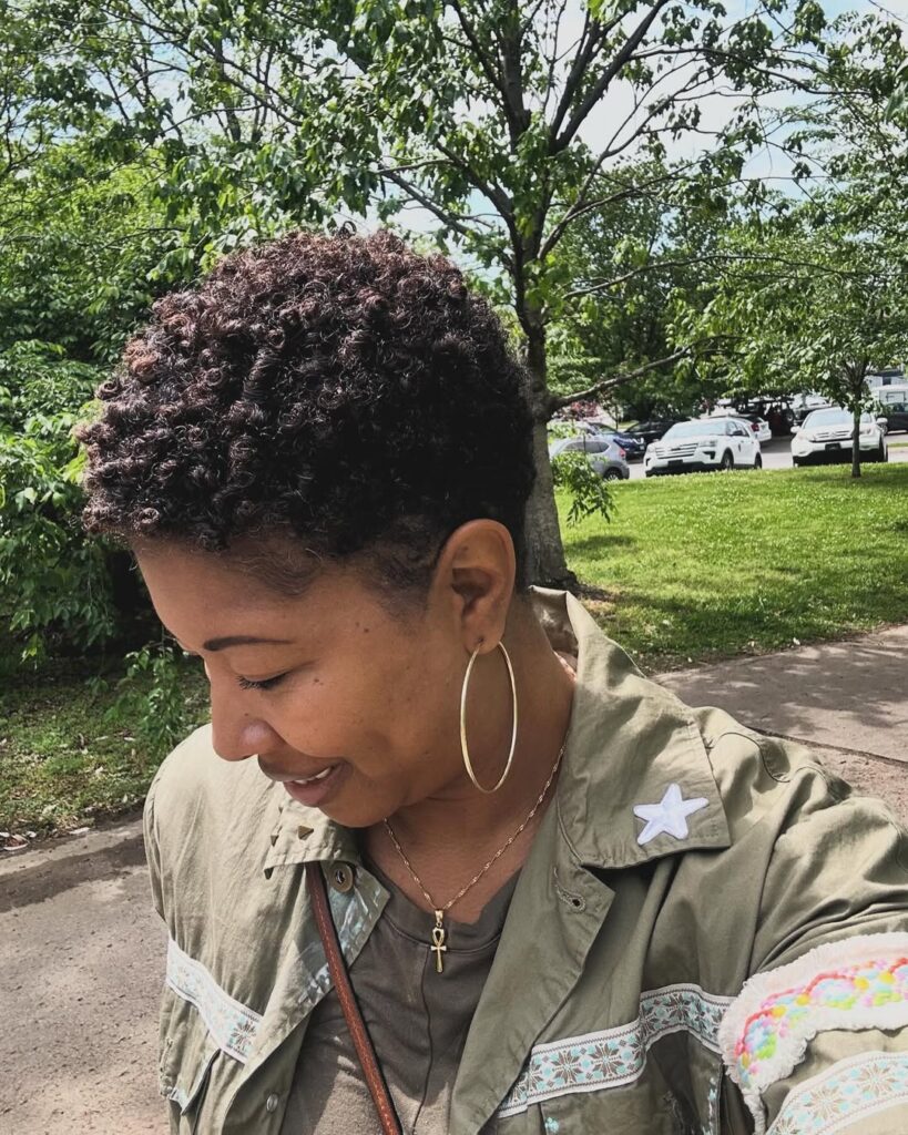 Mulher negra com cabelo bixie, crespo e preto com iluminação ruiva