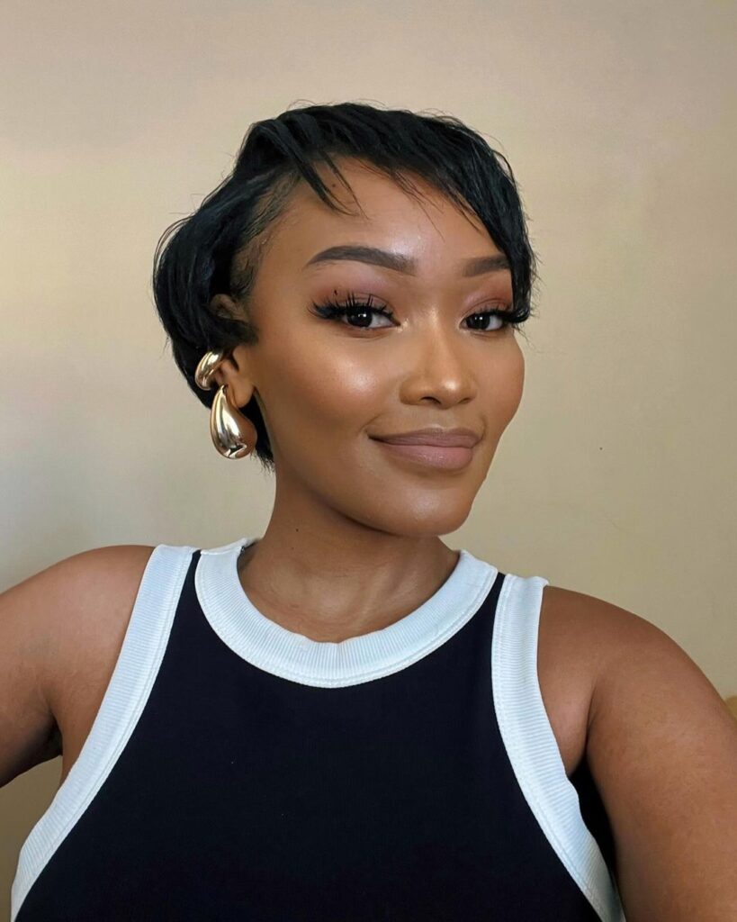Mulher negra com cabelo bixie, liso e preto, usando regata preta e brinco dourado