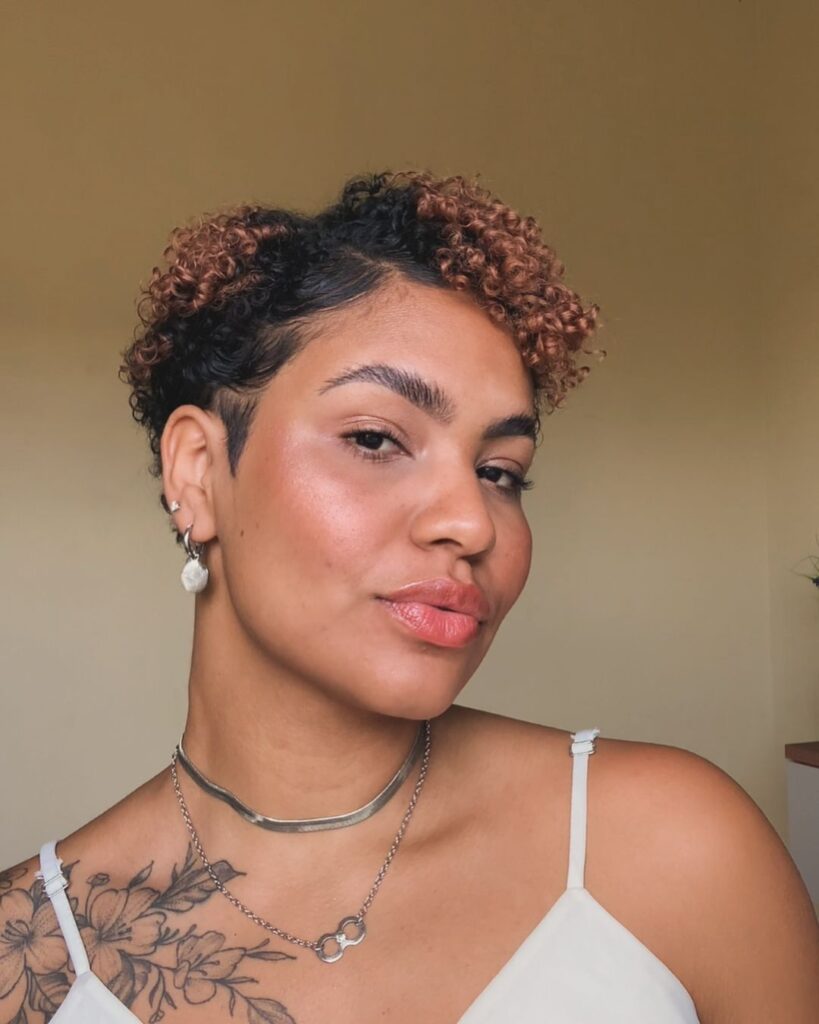 Mulher negra com cabelo bixie, crespo e preto com iluminação castanha