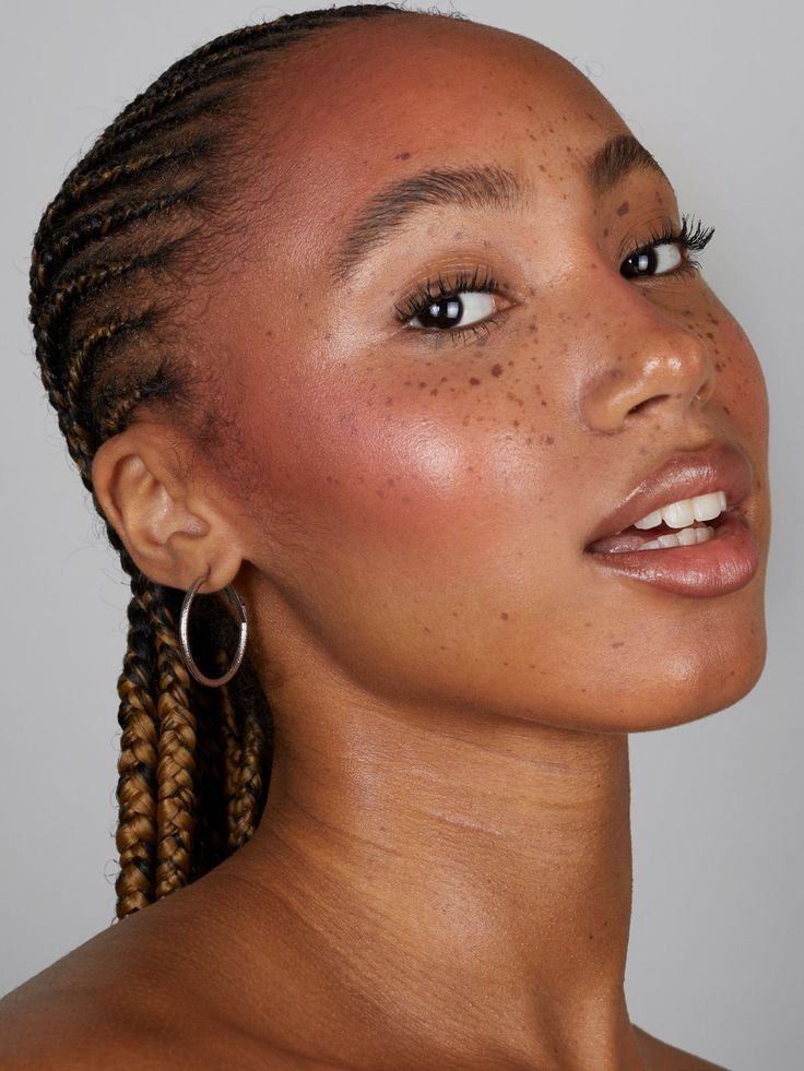 Mulher de pele preta, com acessórios em prata, cabelo trançado e maquiagem plum