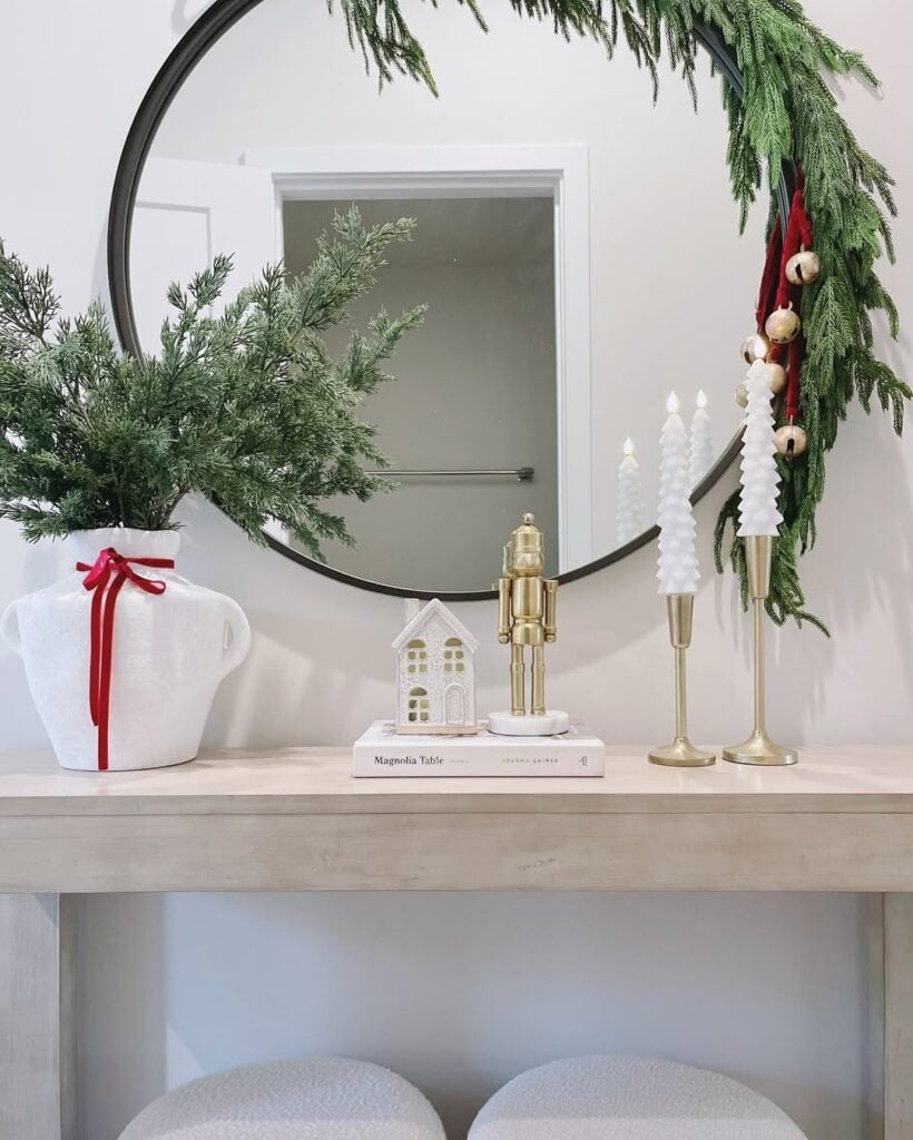 Aparador com decoração natalina, com casa enfeitada, vaso de plantas com laço, livro e velas