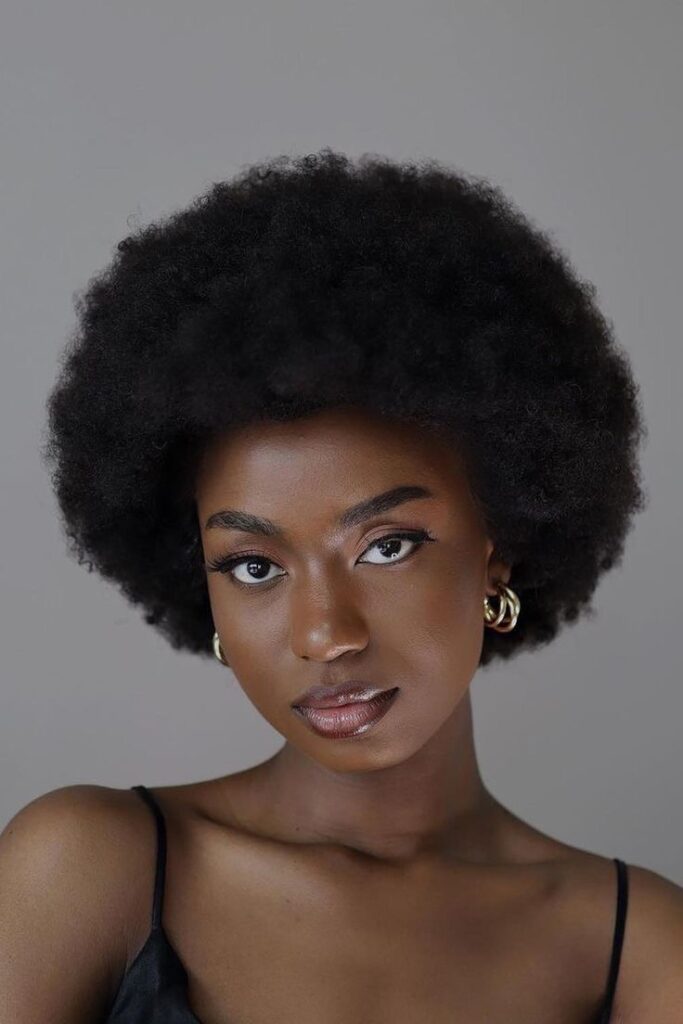 Mulher de pele preta, com regata preta, cabelo escuro black, acessórios em dourado e sobrancelha preenchida
