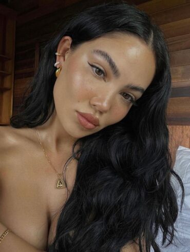 Mulher de pele branca, com cabelo escuro ondulado, acessórios em dourado e maquiagem fresh