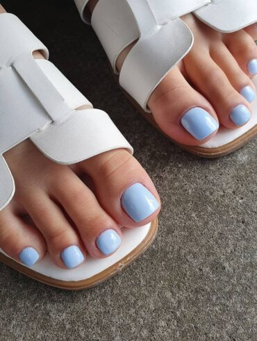Pés de pele branca, com calçado branco e unhas azul-claro