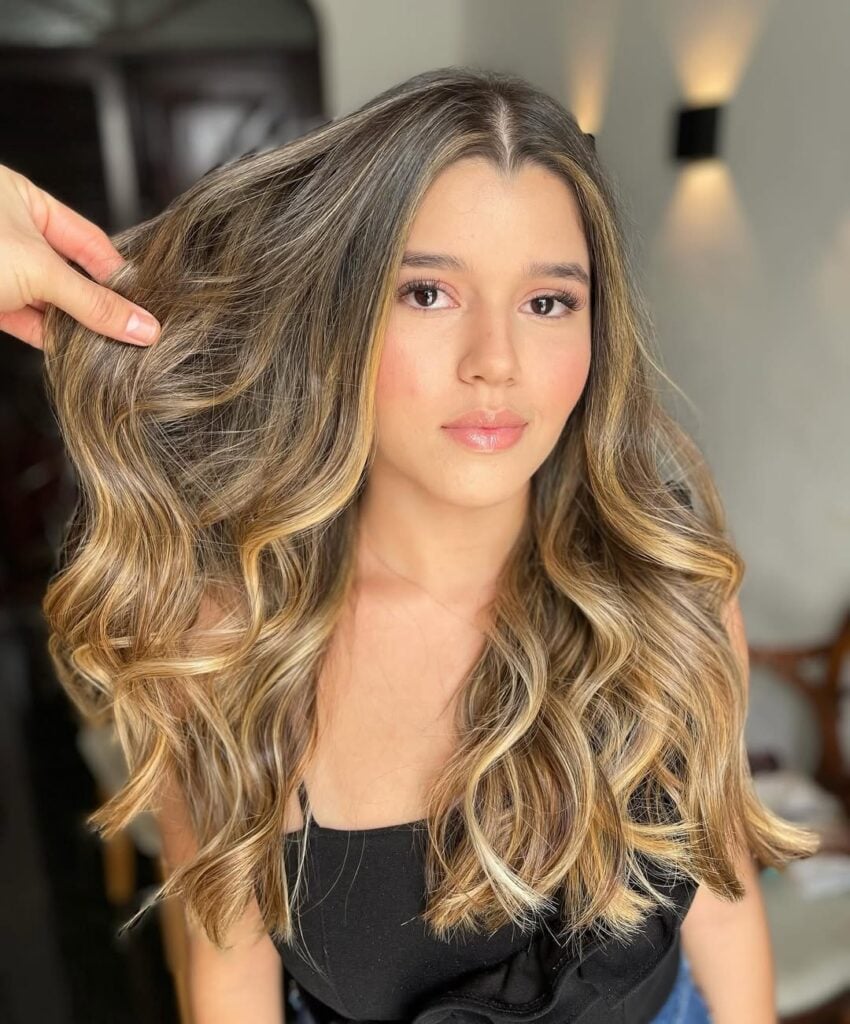 Mulher branca, com cabelo longo e ondulado, com efeito loiro iluminado