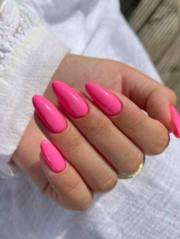 Mão de pele branca, com acessórios em dourado e unha amendoada hot pink