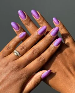 Mãos de pele preta, sobrepostas, com anel em prata e unha amendoada com esmalte roxo e glitter