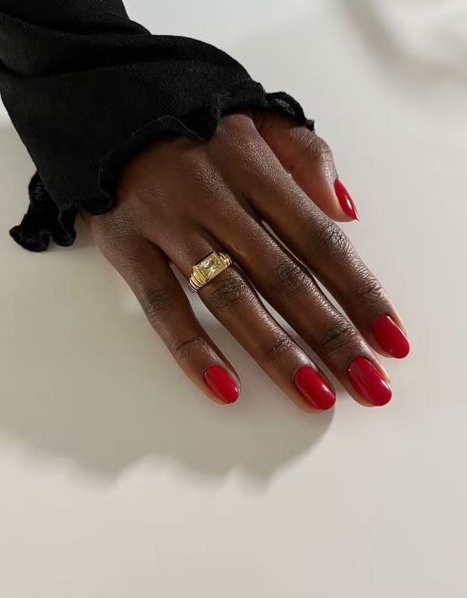 Mão de pele preta, com anel em dourado e unha amendoada vermelha 