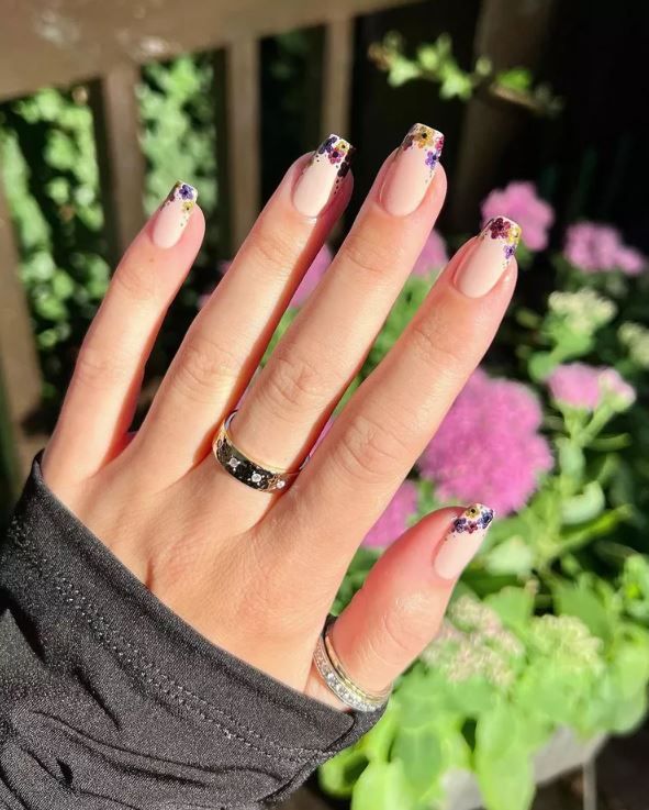 Mão de pele branca, com acessório em dourado e unha bailarina com francesinha de flores