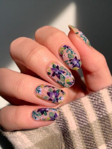 Mão de pele branca, com unha amendoada decorada com flores roxas e verdes