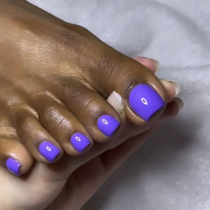 Pé de pele preta com unha roxo vibrante 