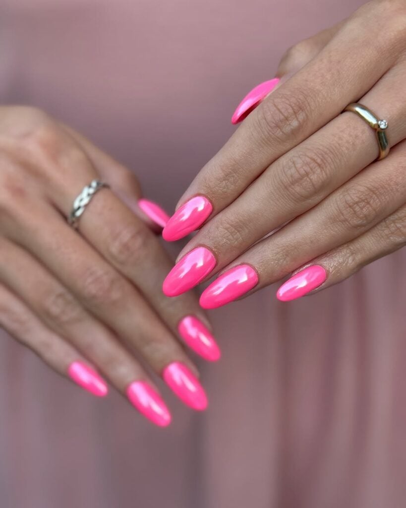 Mãos branca, com acessórios em prata e unha amendoada hot pink cromada 